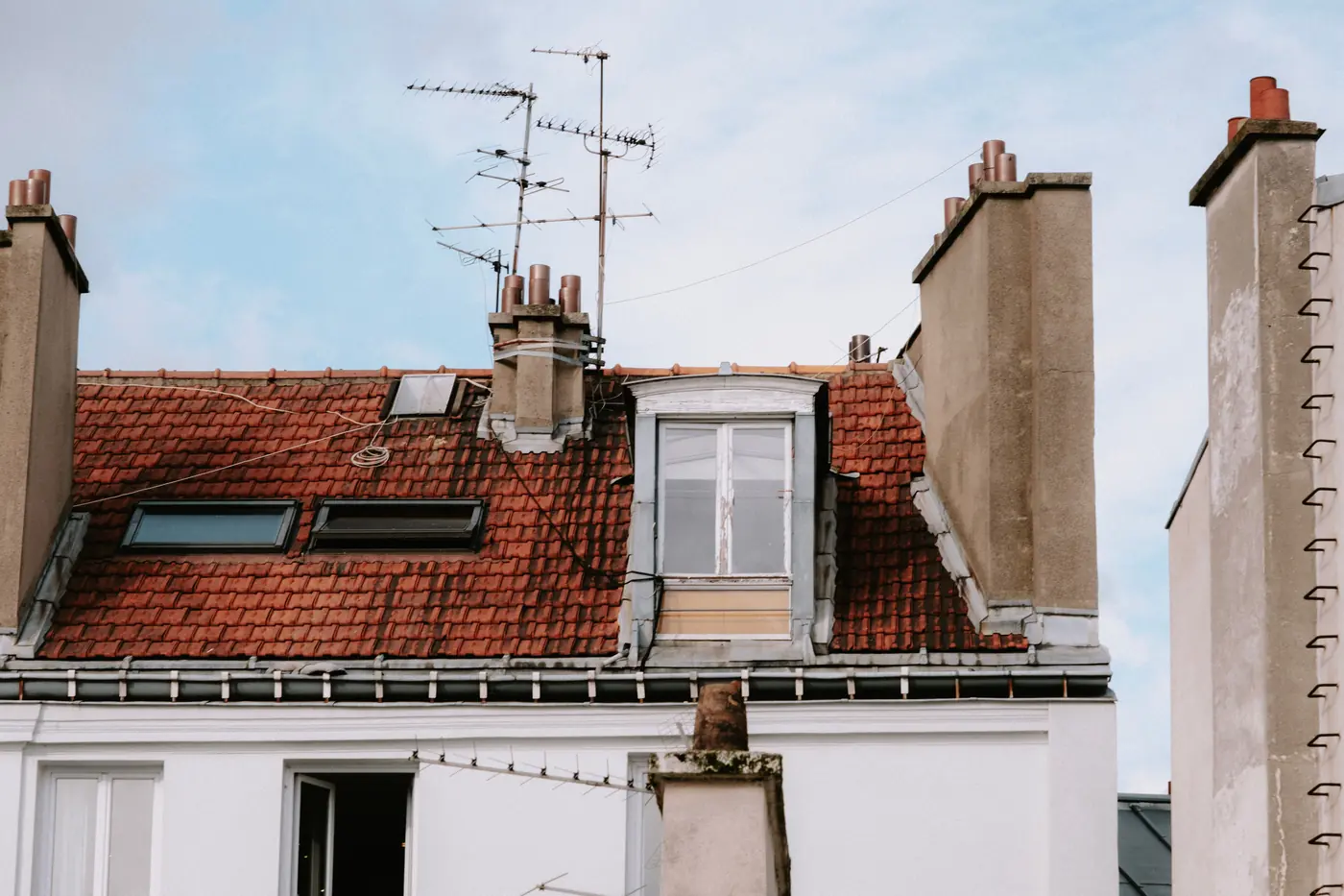 Toiture en tuiles rouges avec plusieurs fenêtres de toit et une lucarne, entre des souches de cheminée