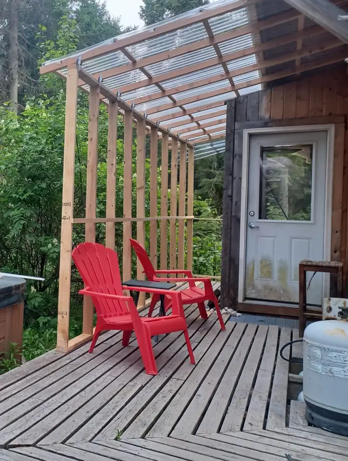 Terrasse en bois couverte d'un toit translucide, avec deux fauteuils rouges