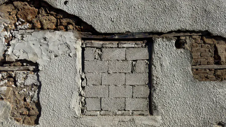 Pan de façade dont le crépi est tombé et laisse voir les pierres, le bois et les blocs du mur