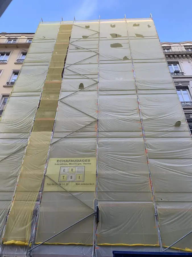 Immeuble couvert d'un échafaudage et d'une bâche pour un ravalement de façade