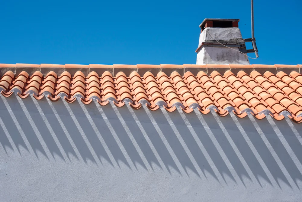 Toit en tuiles à emboîtement avec une cheminée sous un ciel bleu